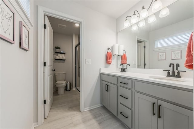 bathroom with double vanity, toilet, a stall shower, baseboards, and wood finished floors