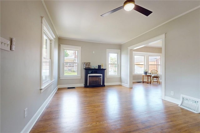 living area featuring ornamental molding, a ceiling fan, wood finished floors, baseboards, and a fireplace