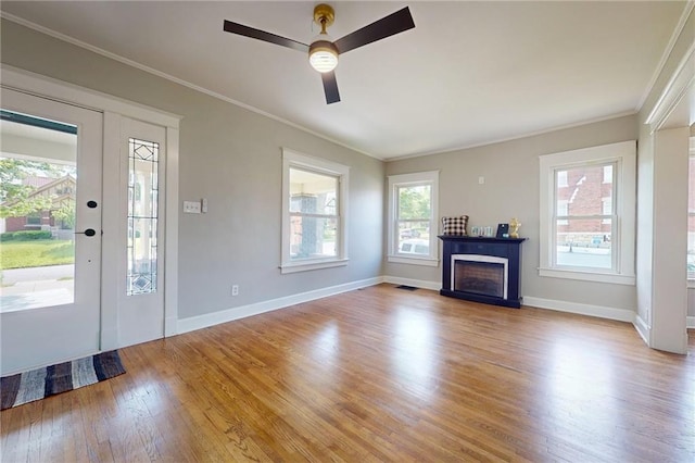 unfurnished living room with wood finished floors, ornamental molding, a ceiling fan, baseboards, and a fireplace