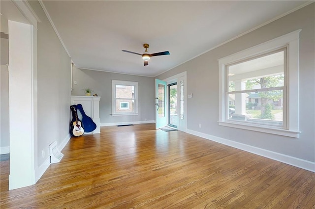 unfurnished living room featuring light wood finished floors, ornamental molding, a ceiling fan, and baseboards