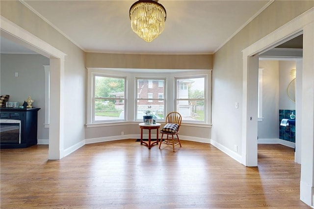 living area featuring wood finished floors, ornamental molding, a chandelier, and baseboards