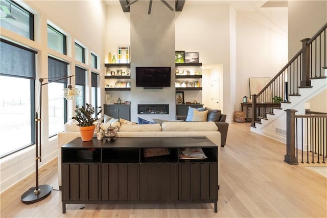 17328 Richards St, Overland Park, KS 66221 - living room with a towering ceiling, a glass covered fireplace, healthy amount of natural light, light wood-style flooring, and stairway