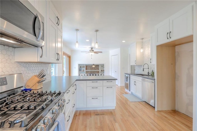 kitchen with appliances with stainless steel finishes, a sink, a peninsula, decorative backsplash, and white cabinets