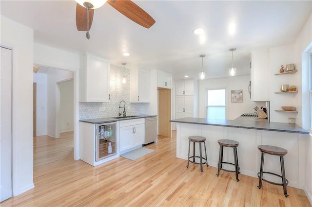 kitchen with dishwasher, dark countertops, a sink, open shelves, and a peninsula