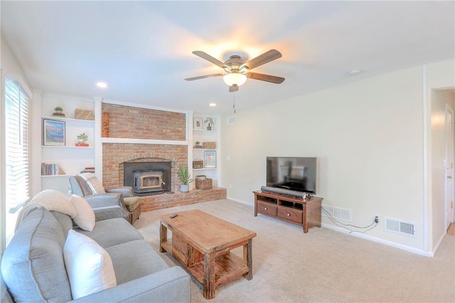 living room with light carpet, a ceiling fan, baseboards, built in shelves, and a wood stove