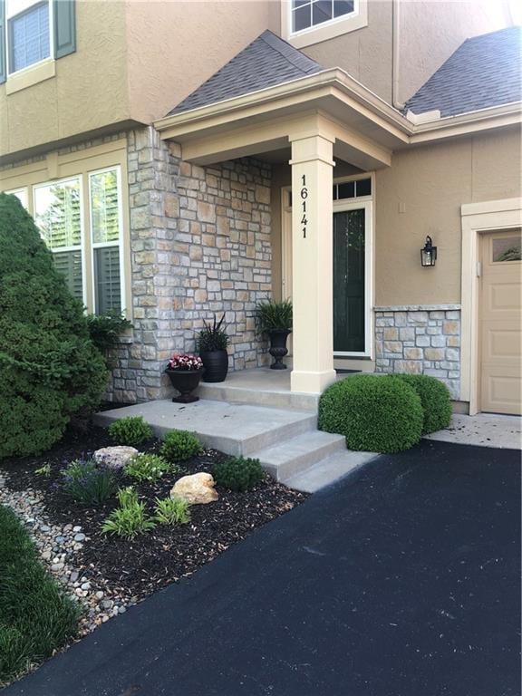 16141 Linden St, Stilwell, KS 66085 - view of exterior entry with stone siding, stucco siding, a shingled roof, and a garage