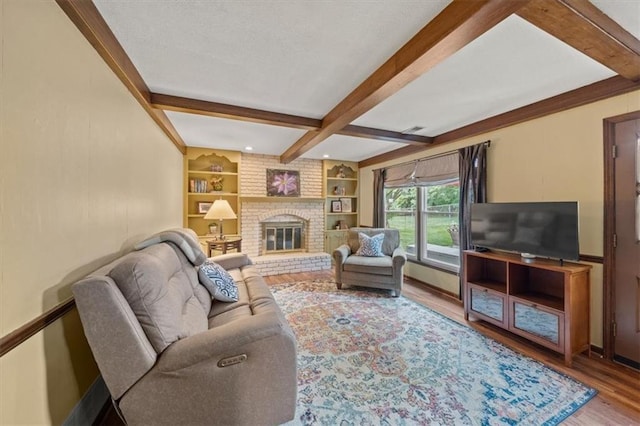 living room featuring beam ceiling, wood finished floors, a fireplace, and built in shelves