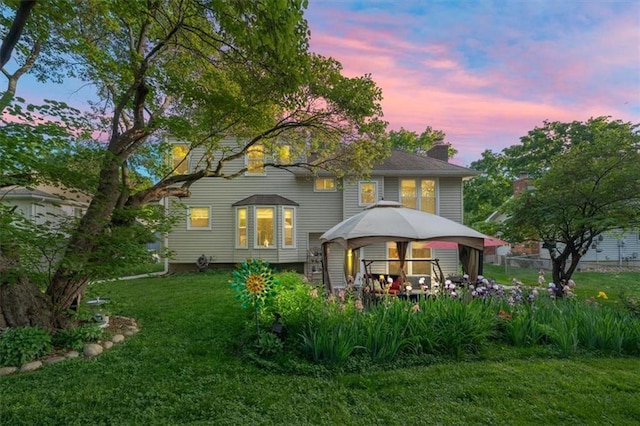 back of property at dusk featuring a gazebo, a lawn, and a chimney