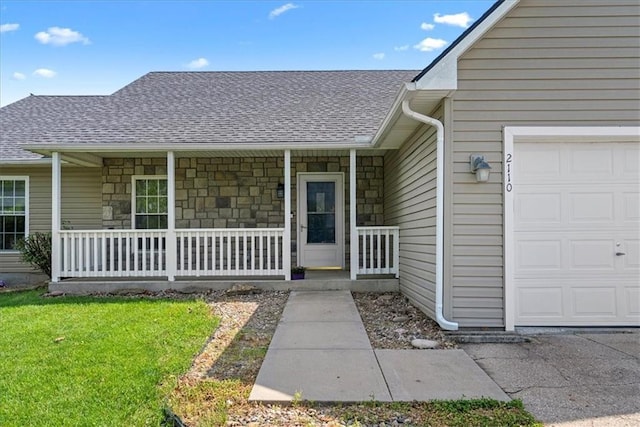 doorway to property with a porch, a garage, a shingled roof, stone siding, and a lawn