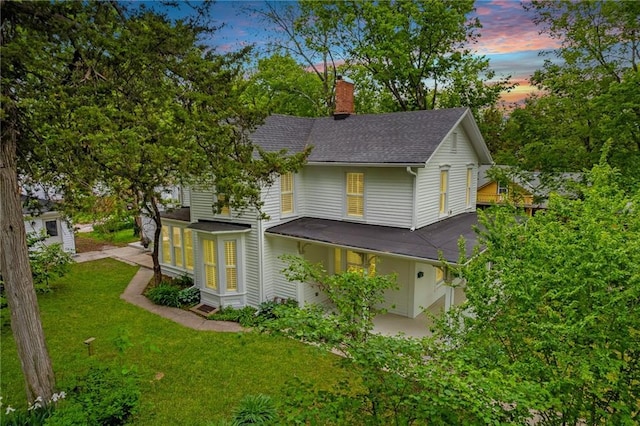 property exterior at dusk featuring a chimney, a lawn, and roof with shingles
