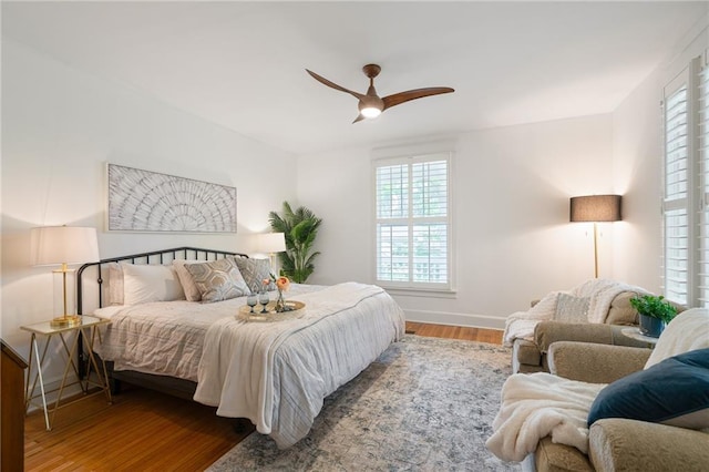 bedroom with multiple windows, wood finished floors, baseboards, and a ceiling fan