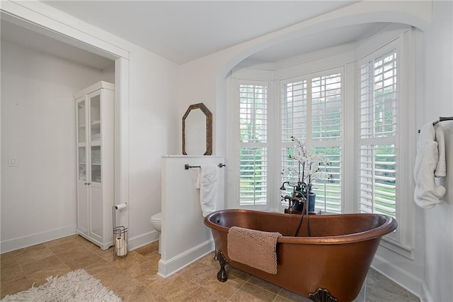 full bathroom featuring a freestanding bath, toilet, and baseboards