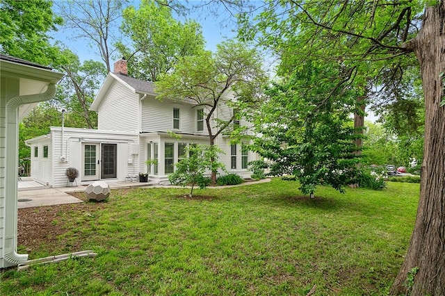 rear view of property with french doors, a chimney, a patio, and a lawn