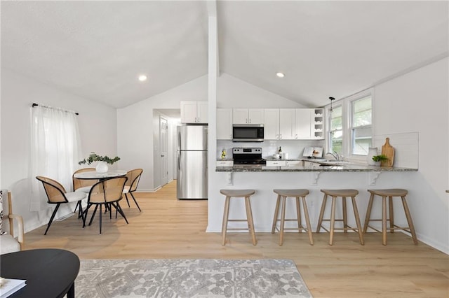 kitchen featuring appliances with stainless steel finishes, dark stone counters, light wood finished floors, a breakfast bar, and recessed lighting