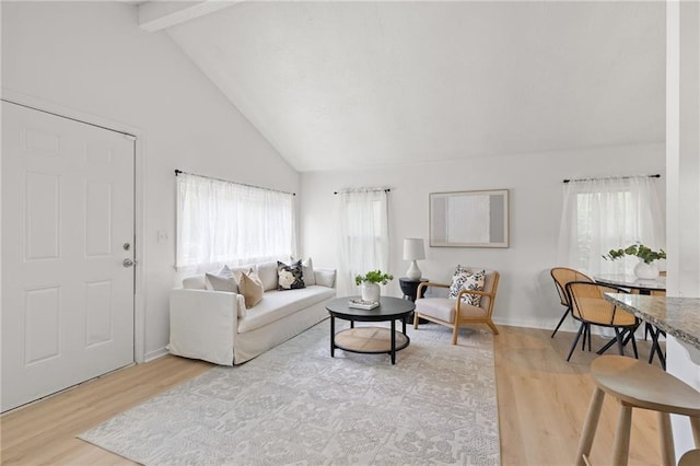 living area with wood finished floors, beam ceiling, healthy amount of natural light, high vaulted ceiling, and baseboards