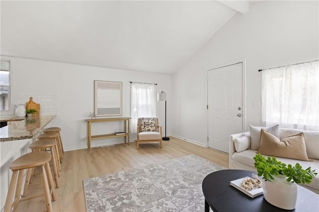 living room with light wood-style flooring, beam ceiling, baseboards, and high vaulted ceiling