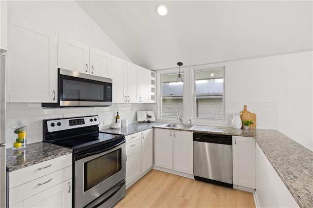 kitchen featuring appliances with stainless steel finishes, a sink, lofted ceiling, tasteful backsplash, and white cabinets