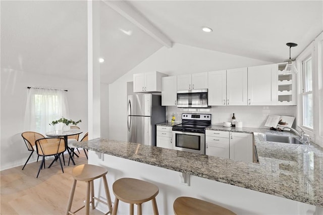 kitchen featuring stainless steel appliances, a sink, a peninsula, white cabinetry, and decorative backsplash