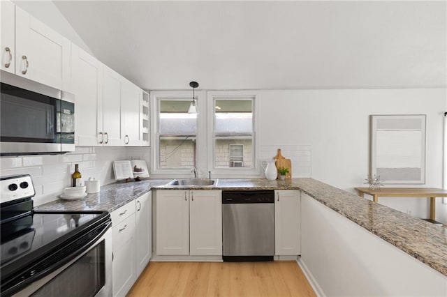 kitchen with appliances with stainless steel finishes, a sink, light wood-style floors, tasteful backsplash, and white cabinetry