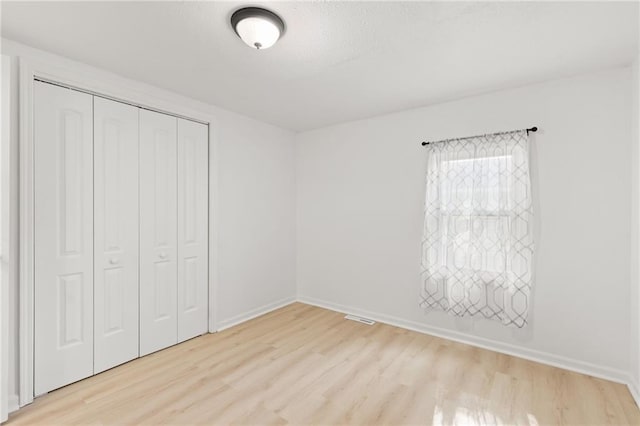unfurnished bedroom featuring light wood-type flooring, a closet, and baseboards