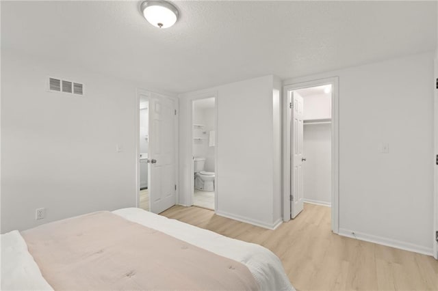 bedroom with wood finished floors, a walk in closet, baseboards, connected bathroom, and a closet