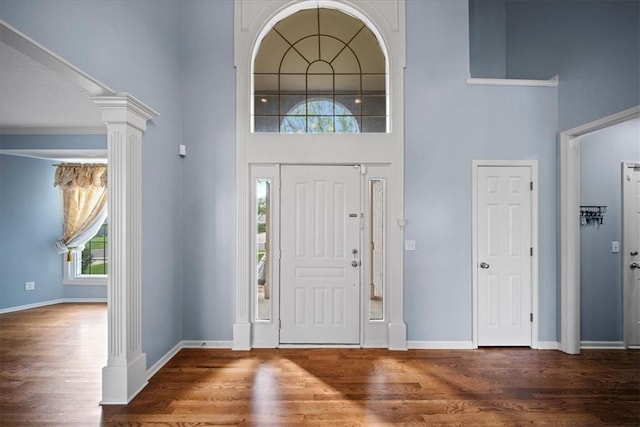 foyer entrance with a high ceiling, ornate columns, wood finished floors, and baseboards