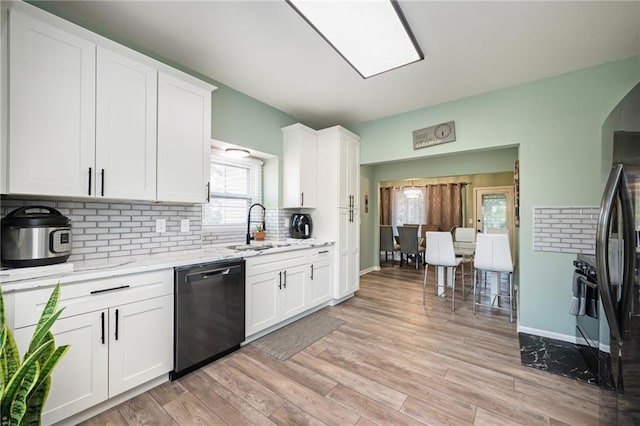 kitchen with dishwasher, a sink, white cabinetry, decorative backsplash, and light stone counters