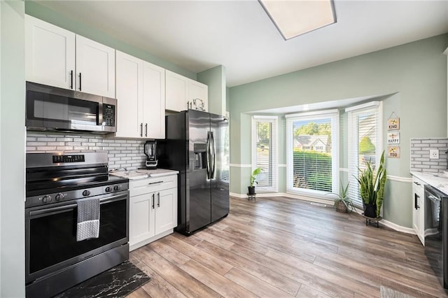 kitchen featuring stainless steel appliances, tasteful backsplash, white cabinets, light wood-style flooring, and baseboards
