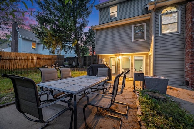 patio terrace at dusk featuring outdoor dining space and fence