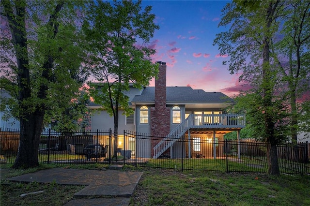 back of house at dusk with stairway, a wooden deck, and a chimney