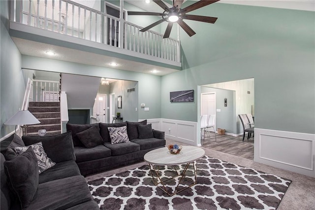 18213 Cliff Dr, Independence, MO 64055 - living room featuring a high ceiling, stairs, a ceiling fan, a decorative wall, and wainscoting