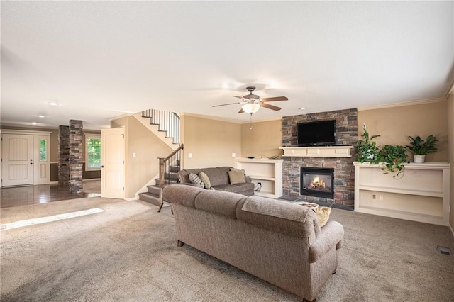 living area featuring carpet, a fireplace, stairs, a ceiling fan, and ornamental molding