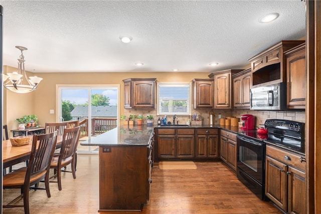 kitchen featuring black / electric stove, stainless steel microwave, dark countertops, a sink, and a chandelier
