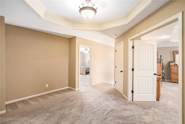 hall featuring ornamental molding, carpet floors, baseboards, and a tray ceiling