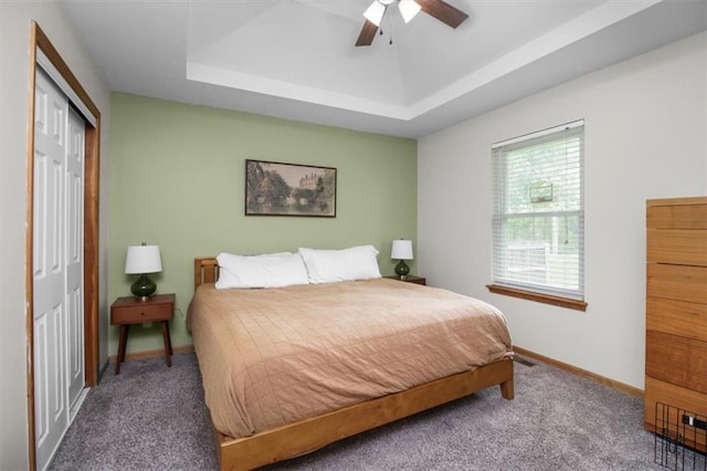 bedroom featuring carpet flooring, a closet, a tray ceiling, and baseboards
