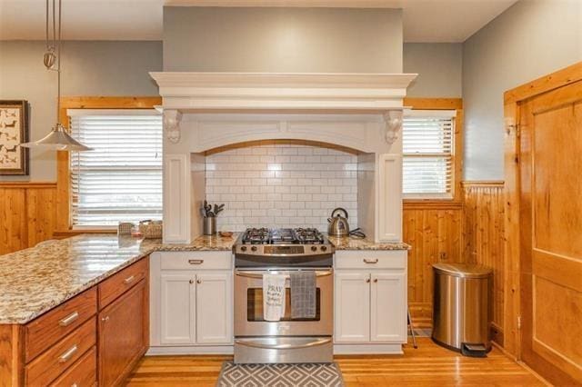 3744 Walnut St, Kansas City, MO 64111 - kitchen featuring stainless steel gas range oven, a wainscoted wall, light wood-style floors, healthy amount of natural light, and light stone counters