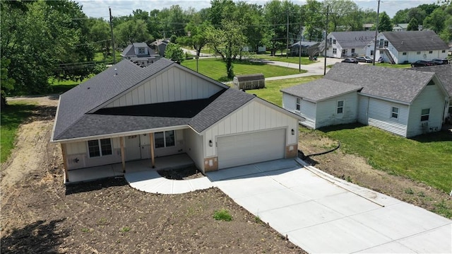 view of front facade with board and batten siding, a garage, concrete driveway, roof with shingles, and a front lawn