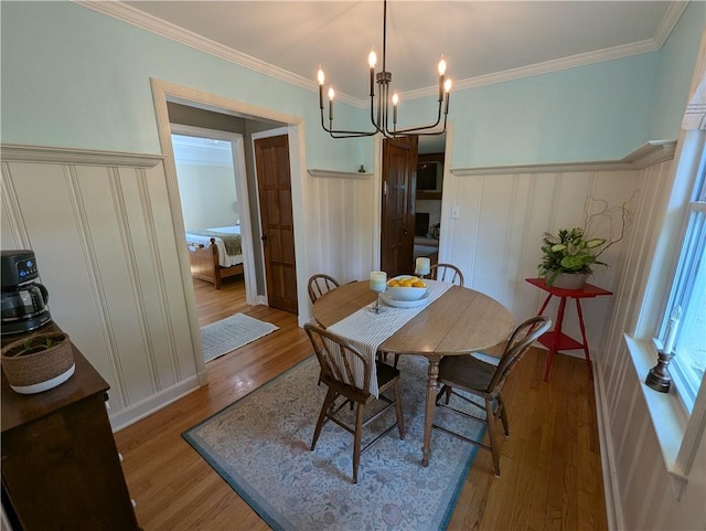 dining space with light wood-type flooring, a chandelier, a wainscoted wall, ornamental molding, and a decorative wall