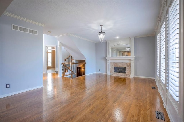 unfurnished living room featuring wood finished floors, a chandelier, stairs, baseboards, and crown molding