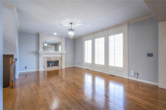 unfurnished living room featuring a high end fireplace, a chandelier, wood finished floors, crown molding, and baseboards