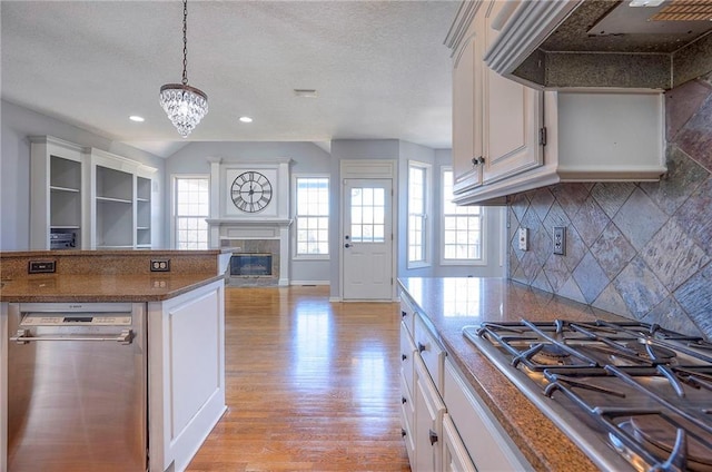kitchen featuring appliances with stainless steel finishes, ventilation hood, a high end fireplace, light wood-style floors, and a chandelier