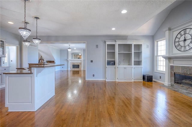 unfurnished living room featuring a tiled fireplace, a textured ceiling, wood finished floors, baseboards, and vaulted ceiling