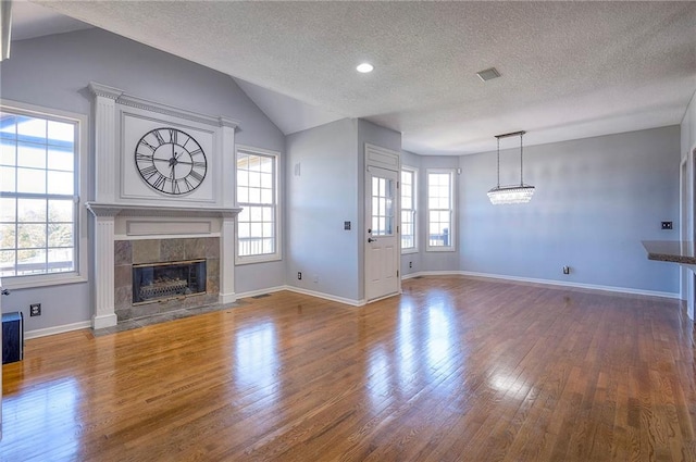 unfurnished living room with healthy amount of natural light, a textured ceiling, a tiled fireplace, wood finished floors, and vaulted ceiling