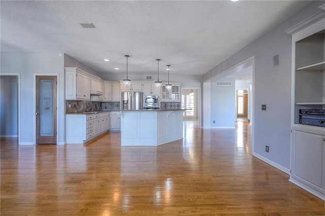 kitchen featuring appliances with stainless steel finishes, white cabinetry, wood finished floors, backsplash, and a textured ceiling