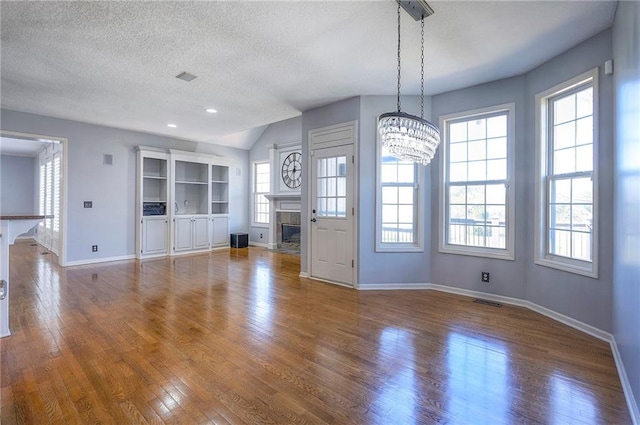 unfurnished dining area featuring a glass covered fireplace, wood finished floors, baseboards, a textured ceiling, and recessed lighting