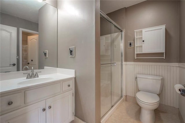 full bath featuring a stall shower, toilet, tile patterned floors, wainscoting, and vanity