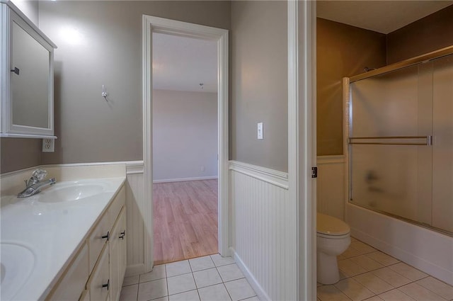 bathroom featuring a wainscoted wall, tile patterned flooring, toilet, double vanity, and enclosed tub / shower combo