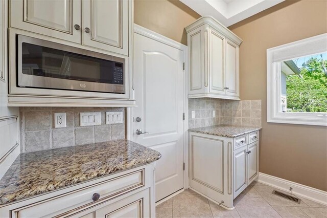 21211 E 34th St S, Independence, MO 64057 - kitchen featuring stainless steel microwave, light stone countertops, decorative backsplash, light tile patterned flooring, and cream cabinets