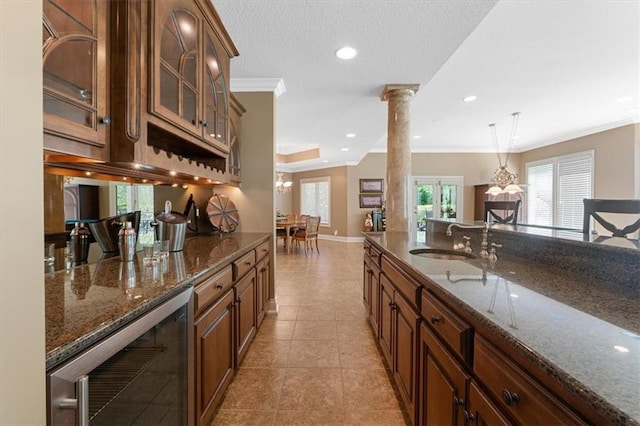 21211 E 34th St S, Independence, MO 64057 - kitchen featuring wine cooler, crown molding, glass insert cabinets, dark stone countertops, and decorative columns