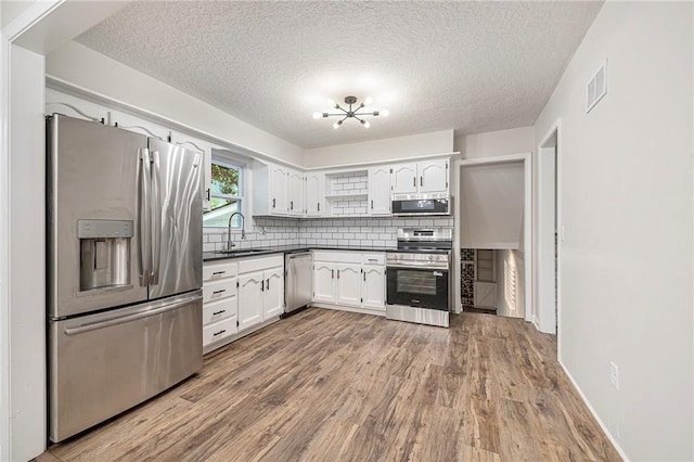 1917 N Concord Rd, Independence, MO 64058 - kitchen with appliances with stainless steel finishes, dark countertops, decorative backsplash, white cabinets, and wood finished floors